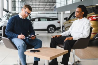 Müşteri erkek, galeride otomobil satın alıyor, araba satıcısıyla kağıt imzalıyor. Galeride yeni otomobil alma kavramı.