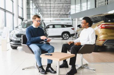 Müşteri erkek, galeride otomobil satın alıyor, araba satıcısıyla kağıt imzalıyor. Galeride yeni otomobil alma kavramı.