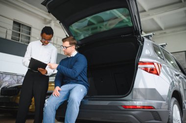 Erkek müşterinin portresi galeride profesyonel araba satıcısıyla konuşuyor. Yeni otomobil seçimi ve satın alma kavramı.