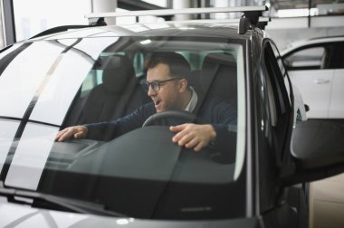 Genç adam yeni bir araç içinde araba Bayilik seçmektir.