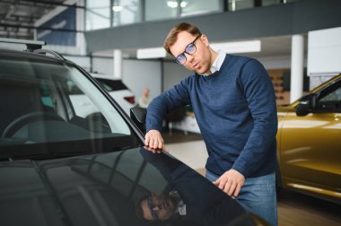 Genç adam yeni bir araç içinde araba Bayilik seçmektir.