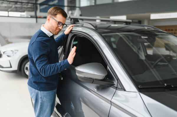 Young man is choosing a new vehicle in car dealership.