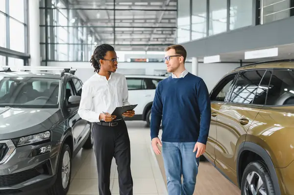 Erkek araba satıcısı, galeride dalgın genç bir müşteriyle sohbet ediyor. Satış merkezinden araba alırken adam dinliyor.