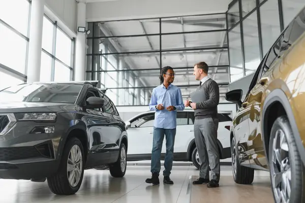 Erkek müşterinin portresi galeride profesyonel araba satıcısıyla konuşuyor. Yeni otomobil seçimi ve satın alma kavramı.