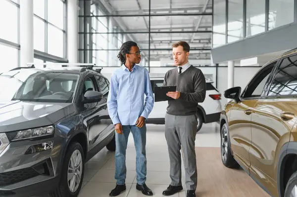 Erkek müşterinin portresi galeride profesyonel araba satıcısıyla konuşuyor. Yeni otomobil seçimi ve satın alma kavramı.