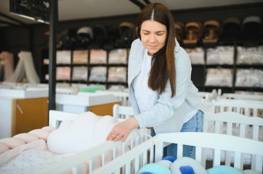 Gülümseyen hamile kadın alışveriş merkezinde bebek beşiği seçiyor..