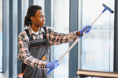 Profesyonel bir işçi uzun ofis pencerelerini temizlemek için cam sileceği kullanıyor, bakım ve temizlik konusunda uzmanlık gösteriyor