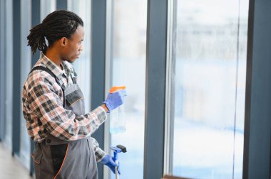 Modern bir ofis binasının camlarını temizleyen genç adam, sprey şişesi ve cam sileceği kullanarak seri ve pırıl pırıl bir bitiş elde etti.