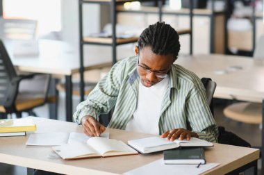 Üniversite kütüphanesinde ders kitapları okurken notlar yazan genç adam, sınavlara ve mezuniyete hazırlanıyor