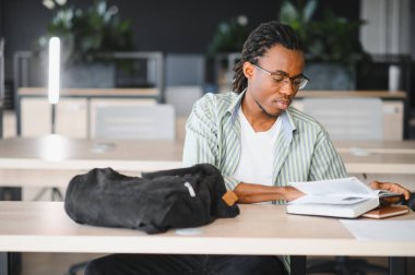 Genç adam bir üniversite kütüphanesinde ders kitabı okumaya daldı, gelecek sınavlara özenle hazırlanıyor ve bilgisini derinleştiriyor.