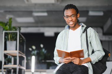 Parlak bir üniversite kütüphanesinde kitap okuyan, sınavlara hazırlanan ve eğitiminden zevk alan gülümseyen Afro-Amerikan bir öğrencinin portresi.
