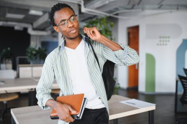 Modern bir üniversite ortamında odaklanmış Afrikalı Amerikalı öğrenci, kitap ve sırt çantası taşıyor, akademik başarıyı ve gelecekteki hedefleri simgeliyor.