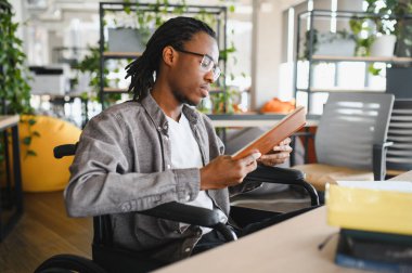 Modern, bitki dolu bir çalışma alanında tekerlekli sandalyede tablet kullanan Afrikalı Amerikalı öğrenci, öğrenme ve eğitime odaklandı.