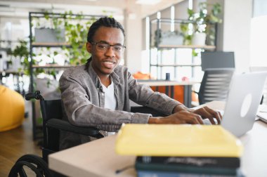 Modern ofis ortamında dizüstü bilgisayar kullanan engelli genç bir adam kararlılığını gösteriyor ve derslerine odaklanıyor.