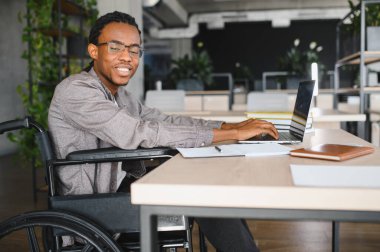 Özürlü ve daktilo kullanan, üniversite kütüphanesinde dizüstü bilgisayar kullanan, eğitiminden zevk alan mutlu genç bir adam.