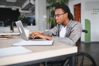 Özürlü genç bir siyahi profesyonel, bilgisayarla çalışıyor, parlak, modern bir ofiste, işyerinde dahil olma ve erişilebilirliği gösteriyor.