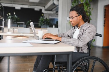 Özürlü genç adam modern ofiste dizüstü bilgisayarla çalışıyor, iş yerinde dahil olma ve erişilebilirlik gösteriyor