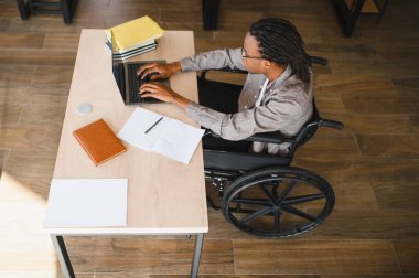 Özürlü genç bir adam dizüstü bilgisayarına odaklanıyor, parlak, çağdaş bir ofis alanında çalışıyor.