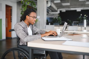 Özürlü genç adam, modern ofiste dizüstü bilgisayarla çalışıyor, işyerine dahil edilme ve erişilebilirlik gösteriyor