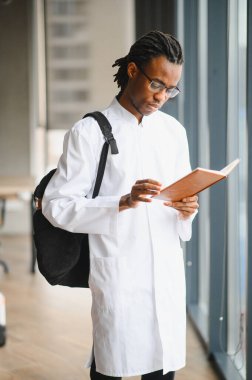 Çalışmaya dalmış, üniversite koridorunda elinde bir kitap tutan kendini adamış tıp öğrencisi, eğitimi, eğitimi ve akademik başarıyı sembolize ediyor.