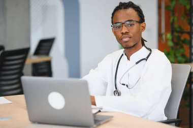 Modern tıp ofisinde dizüstü bilgisayar kullanan kendine güvenen bir doktor profesyonellik ve sağlık teknolojisi sergiliyor.