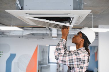 Hvac teknisyeni, ofis ortamında en iyi performansı sağlayan, tavana monte edilmiş bir kaset klima ünitesini denetliyor ve onarıyor.