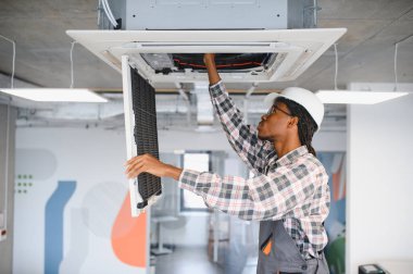 Afrikalı Amerikan hvac teknisyeni modern bir ofiste bakım sırasında klima filtresi kontrol ediyor.