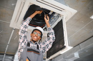 Profesyonel teknisyen tavan havalandırma ünitesinde çalışıyor. Verimli havalandırma ve soğutma sağlıyor. Güvenlik için koruyucu giysi giyiyor.