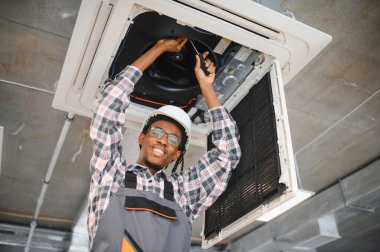 Gülümseyen Afro-Amerikan işçiler içeride havalandırma sistemini tamir ederken, en uygun soğutma ve hava akışını sağlamak için tornavida kullanıyorlar.