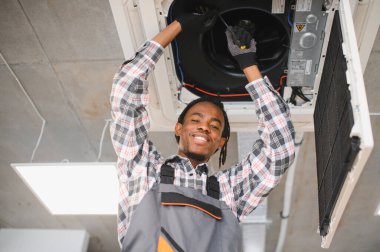 Gülümseyen Afro-Amerikan işçiler bir klima tamir ederken tornavida kullanarak vidayı sıkıyor.