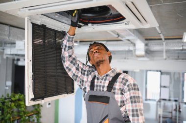 Afrikalı Amerikalı Hvac teknisyeni bir havalandırma ünitesini kontrol ediyor. Modern bir ofis binasının havalandırma sistemini tamir ediyor.