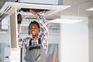 Genç Afro-Amerikan bakım işçisi tornavida kullanarak havalandırma sistemini tamir ediyor.