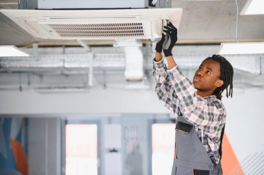 Genç Afrikalı Amerikalı işçi modern bir binanın tavanına klima takıyor.