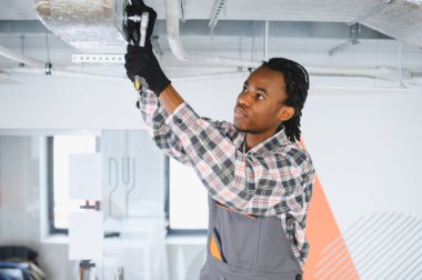 Genç Afrikalı Amerikalı işçi, havalandırma sistemini tamir ediyor, İngiliz anahtarını ustalıkla kullanırken elimizdeki işe odaklanıyor.