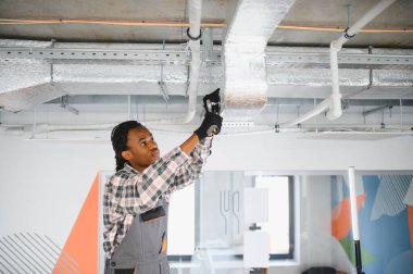 Genç bakım işçisi havalandırma borularını tamir ediyor, uygun havalandırmayı ve rahat bir çalışma alanını sağlıyor.