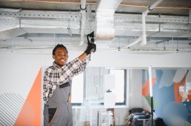 Genç Afro-Amerikan HVK teknisyeni modern bir ofise klima kuruyor ve rahat bir çalışma ortamı sağlıyor.