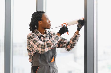 Profesyonel bir işçi cam çerçevesine hava geçirmez yalıtım sağlamak için kabartma tabancası kullanıyor.