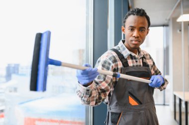 Yüksek katlı bir binanın camlarını silmek için cam sileceği kullanan profesyonel üniformalı bir işçi. Bakım ve temizlik konusunda uzmanlık gösteriyor.