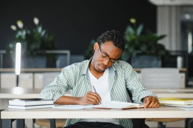 Öğrenim ve akademik büyümeye dalmış, özenle bir üniversite kütüphanesinde okurken notlar yazan Afrikalı Amerikalı genç bir öğrenci.