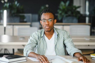 Kendini adamış Afrikalı Amerikalı öğrenci, kitap ve notlarla özenle çalışıyor, modern bir üniversite ortamında mezuniyete hazırlanıyor.