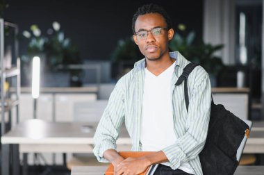 Odaklanmış bir Afro-Amerikan üniversite öğrencisinin portresi kitap ve defter tutuyor, modern bir kütüphanede eğitime ve akademik başarıya hazır.