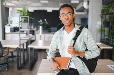 Afrika kökenli Amerikalı tıp öğrencisi, modern bir üniversite ortamında okuyor, kitapları tutuyor ve bir sırt çantası taşıyor, akademik bağlılığı simgeliyor.