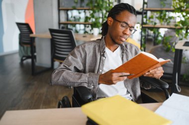 Özürlü genç bir adam okuyup kitap okuyor, üniversite kütüphanesinde ya da sınıfta vakit geçiriyor.