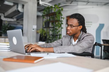 Özürlü genç siyahi profesyonel adam dizüstü bilgisayarda çalışıyor, işe dahil olma ve iş yerinde erişilebilirlik gösteriyor