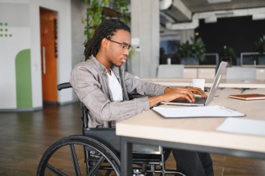 Özürlü genç bir adam dizüstü bilgisayarda çalışıyor, modern işyerine dahil edilme ve erişilebilirlik gösteriyor