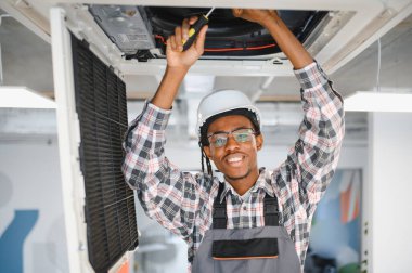 Bir tornavidayla havalandırma sistemini tamir ederken gülümseyen Afrikalı genç bir Amerikalı işçi kapalı alanda en iyi performansı sağlamaya odaklandı.