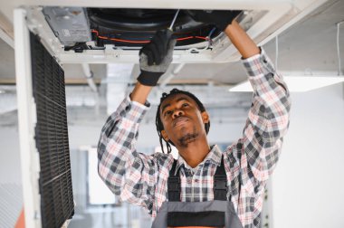 Genç Afro-Amerikan bakım işçisi bir tornavidayla havalandırma sistemini tamir ederken, en uygun soğutma verimliliğini sağlamaya odaklandı.