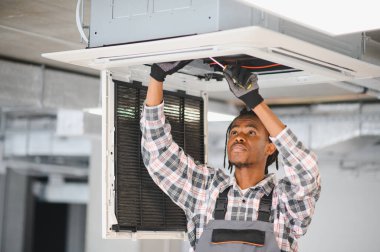 Afrikalı Amerikan hvac teknisyeni tornavida kullanarak havalandırma sistemini tamir ediyor.
