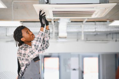 Genç Afro-Amerikan HVK teknisyeni modern bir ofis binasının tavanına klima kuruyor.