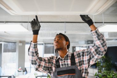 Genç Afro-Amerikan erkek teknisyen havalandırma sistemini inceliyor ve onarıyor.